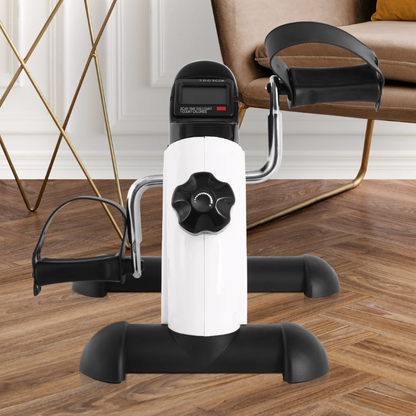 Compact under-desk elliptical trainer with digital display, designed for both leg and arm workouts, placed on a wooden floor next to a chair.