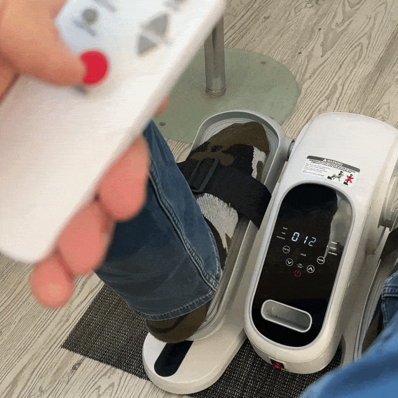 Senior using an under-desk elliptical trainer with a remote control.